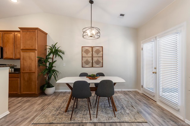 dining area with light hardwood / wood-style floors, a chandelier, and vaulted ceiling