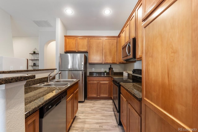 kitchen featuring light hardwood / wood-style floors, sink, stainless steel appliances, and dark stone counters