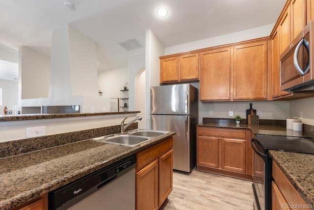 kitchen featuring sink, light hardwood / wood-style flooring, stainless steel appliances, and dark stone countertops