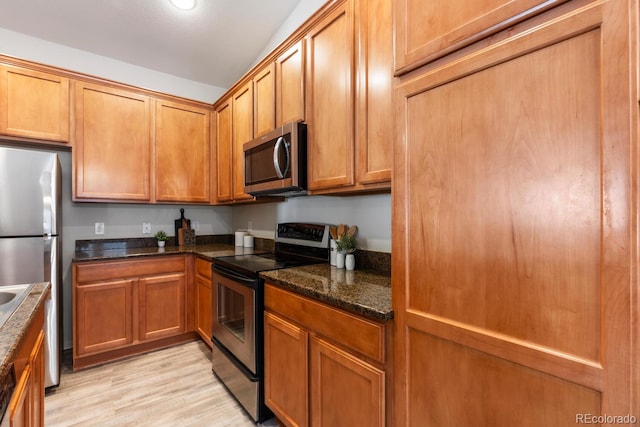 kitchen with dark stone countertops, stainless steel appliances, and light hardwood / wood-style flooring