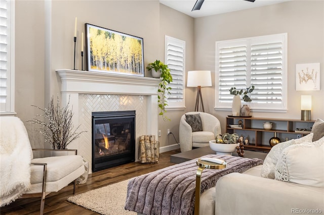 sitting room with dark wood-type flooring, a fireplace, and ceiling fan