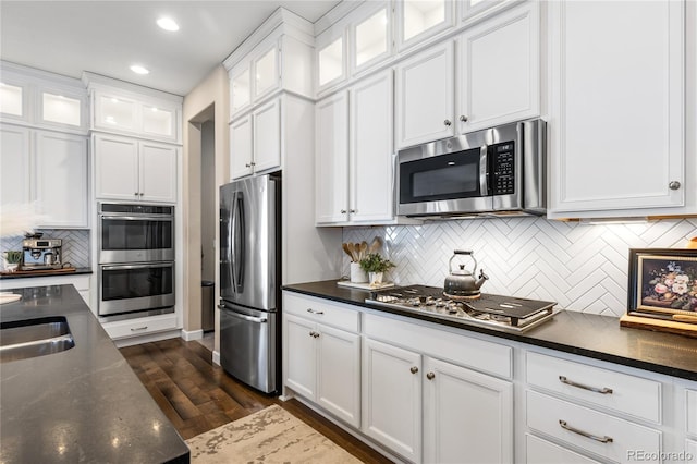 kitchen featuring dark wood-type flooring, appliances with stainless steel finishes, dark stone counters, and white cabinets