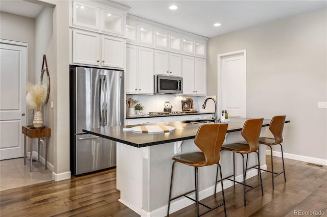 kitchen with tasteful backsplash, dark countertops, a center island with sink, stainless steel appliances, and a sink