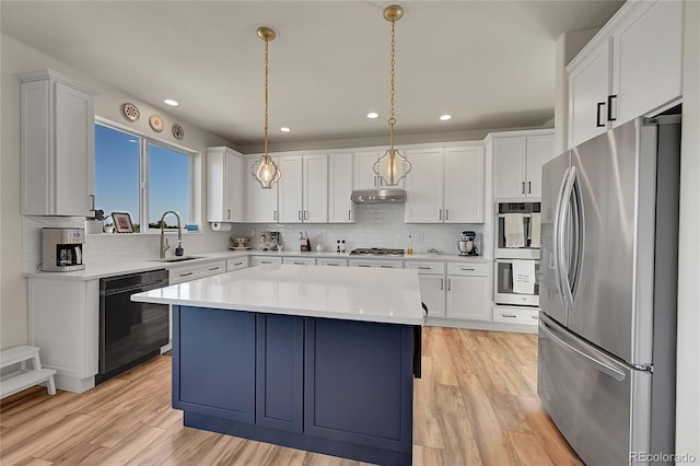 kitchen with a sink, light countertops, light wood-style floors, under cabinet range hood, and appliances with stainless steel finishes