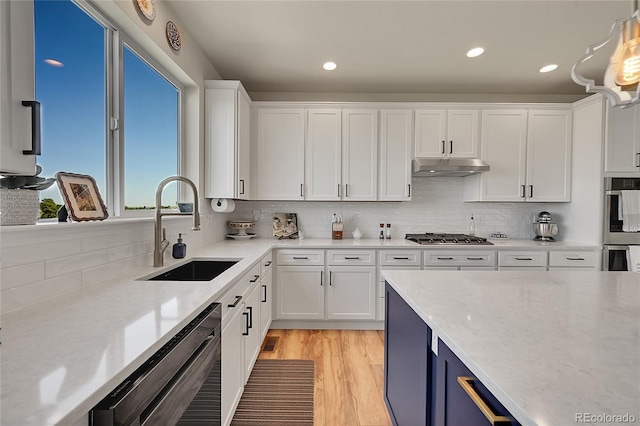 kitchen with a sink, white cabinets, light wood-style floors, appliances with stainless steel finishes, and under cabinet range hood