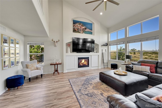 living area featuring a glass covered fireplace, plenty of natural light, high vaulted ceiling, and light wood-style flooring