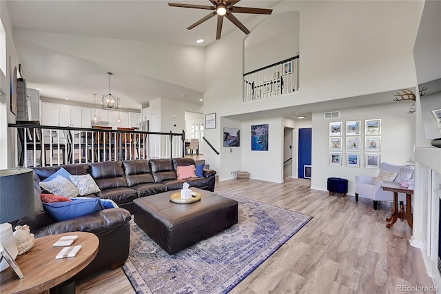 living room featuring light wood-type flooring, visible vents, ceiling fan with notable chandelier, baseboards, and stairs