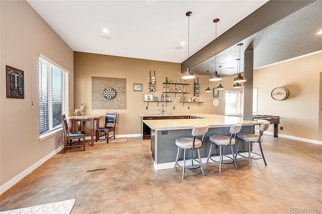 kitchen with light stone counters, a kitchen bar, baseboards, and concrete floors