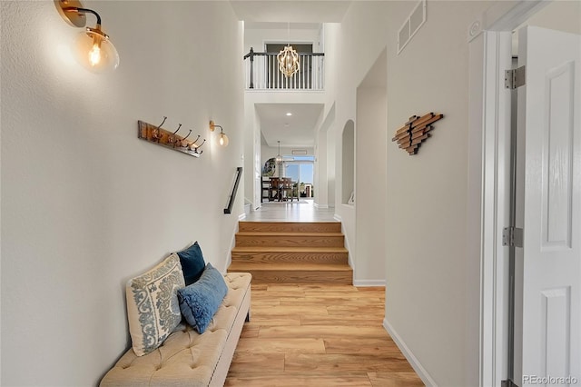 hallway featuring visible vents, stairway, an inviting chandelier, light wood-style floors, and arched walkways