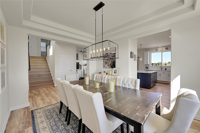 dining area with light wood-type flooring, stairs, a raised ceiling, and baseboards