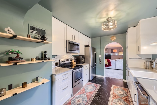6995 W 27th Ave, Wheat Ridge, CO 80033 - kitchen featuring stainless steel appliances, arched walkways, white cabinetry, light countertops, and backsplash