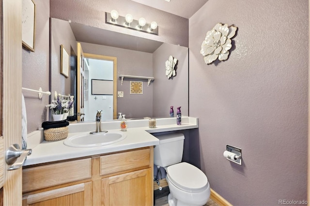 bathroom featuring baseboards, toilet, vanity, and a textured wall