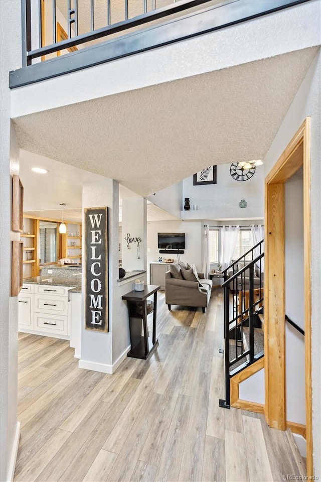 interior space featuring baseboards, stairway, lofted ceiling, light wood-style flooring, and a textured ceiling