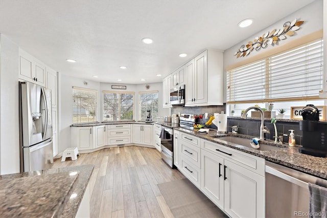 kitchen featuring a sink, stainless steel appliances, dark stone counters, white cabinets, and decorative backsplash