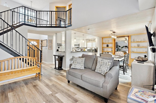 living room with baseboards, a chandelier, stairway, a high ceiling, and light wood-style floors