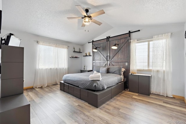 bedroom featuring light wood finished floors, a textured ceiling, a barn door, and vaulted ceiling