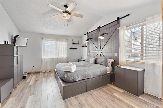 bedroom with a barn door, multiple windows, vaulted ceiling, and light wood finished floors