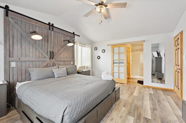 bedroom with light wood-type flooring, a barn door, and lofted ceiling