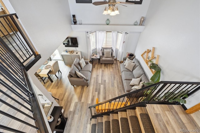 living room with a ceiling fan, a high ceiling, stairs, and wood finished floors