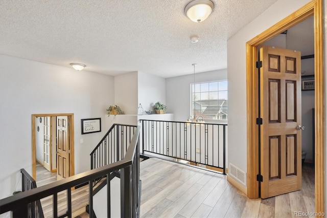 corridor with visible vents, an upstairs landing, a notable chandelier, a textured ceiling, and light wood-style floors