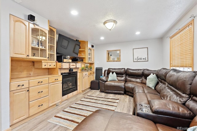 living area with recessed lighting, a textured ceiling, a glass covered fireplace, and light wood finished floors