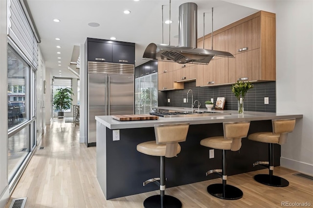 kitchen featuring a peninsula, island exhaust hood, a kitchen bar, built in refrigerator, and modern cabinets