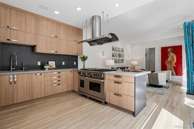 kitchen with a peninsula, open floor plan, range with two ovens, island exhaust hood, and a sink