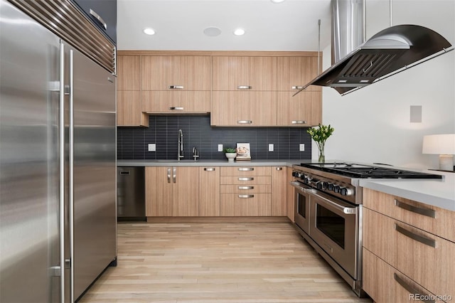 kitchen featuring light brown cabinetry, high quality appliances, a sink, and wall chimney range hood