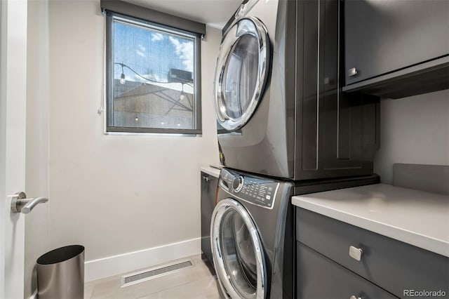 laundry area featuring visible vents, stacked washer and clothes dryer, baseboards, cabinet space, and light tile patterned floors