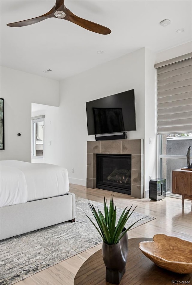 bedroom with ceiling fan, visible vents, a tile fireplace, and wood finished floors