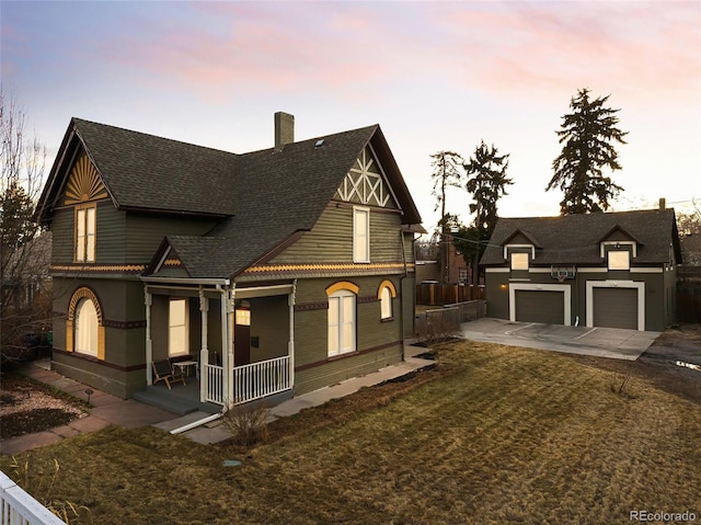 view of front of home featuring roof with shingles, a detached garage, a chimney, a porch, and a front yard