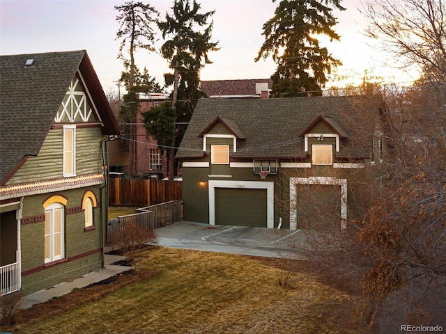 exterior space featuring a garage, concrete driveway, a shingled roof, and fence