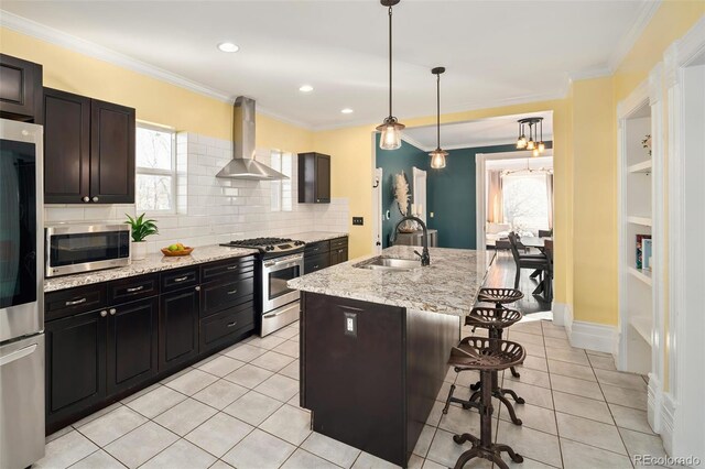 kitchen featuring wall chimney exhaust hood, ornamental molding, a breakfast bar, stainless steel appliances, and a sink