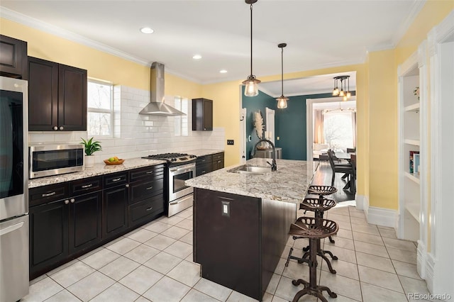 kitchen featuring crown molding, wall chimney exhaust hood, stainless steel appliances, a sink, and a kitchen breakfast bar