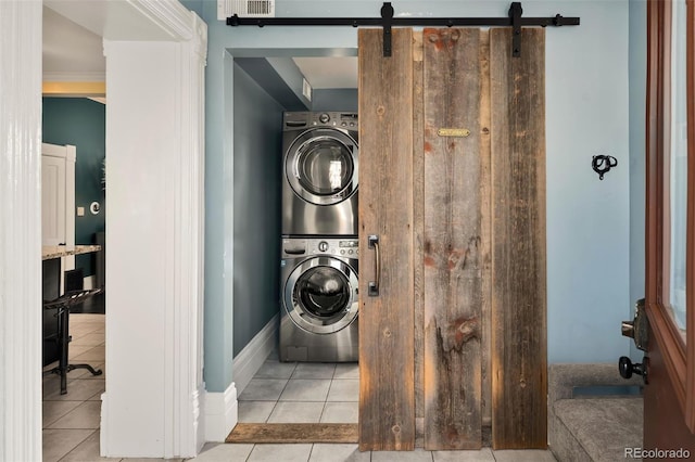 laundry area with stacked washer and dryer, a barn door, laundry area, and tile patterned floors