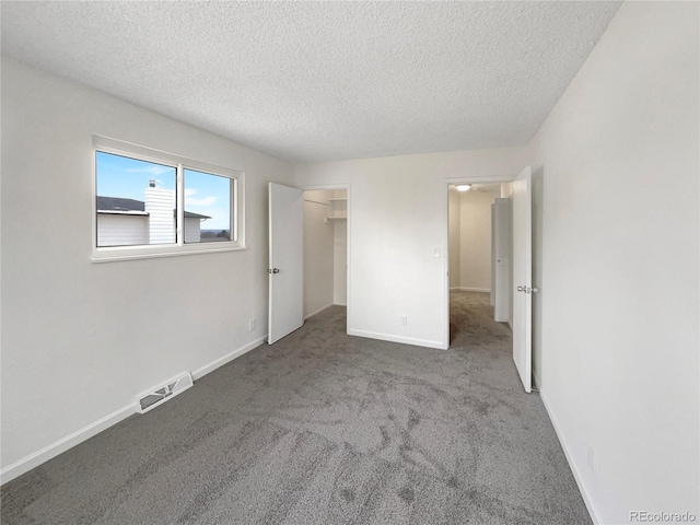 unfurnished bedroom with carpet floors, a textured ceiling, and a walk in closet