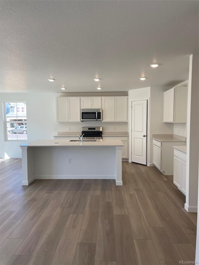 kitchen featuring appliances with stainless steel finishes, light countertops, a kitchen island with sink, dark wood-style floors, and recessed lighting