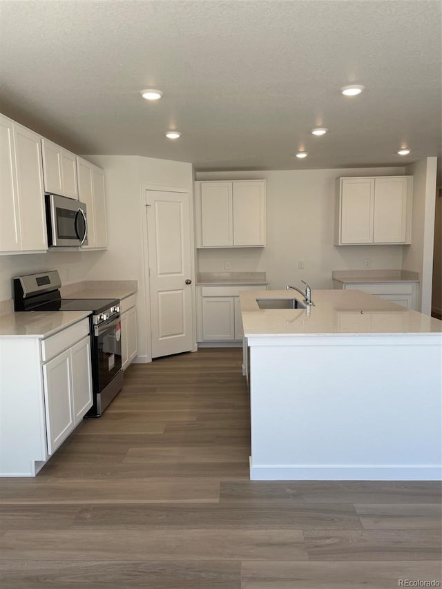 kitchen with stainless steel appliances, a sink, recessed lighting, white cabinets, and a center island with sink
