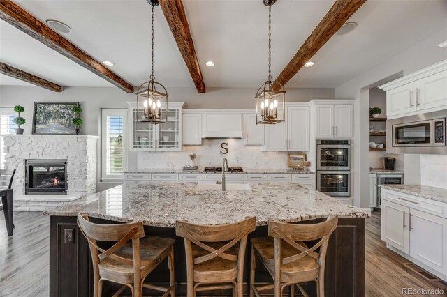 360 Basilwood Way, Highlands Ranch, CO 80126 - kitchen featuring appliances with stainless steel finishes, decorative backsplash, beverage cooler, white cabinets, and a stone fireplace