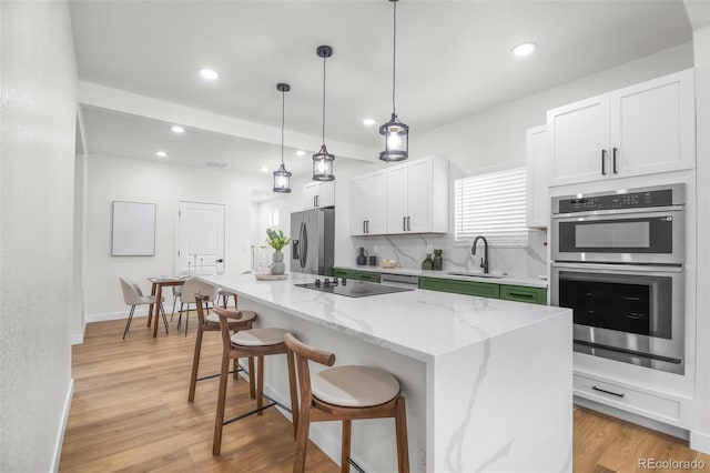 kitchen with appliances with stainless steel finishes, decorative light fixtures, sink, white cabinets, and a center island