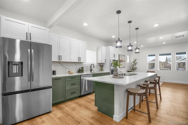 kitchen featuring appliances with stainless steel finishes, white cabinetry, hanging light fixtures, a center island, and light hardwood / wood-style flooring