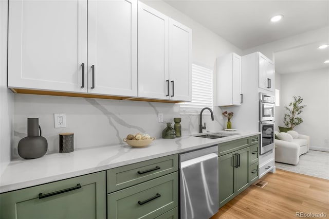 kitchen with sink, green cabinets, white cabinetry, stainless steel appliances, and light wood-type flooring