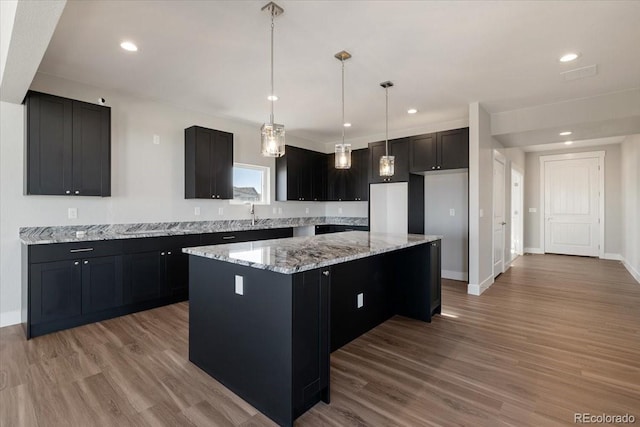 kitchen featuring light stone countertops, a center island, hanging light fixtures, and light wood-type flooring