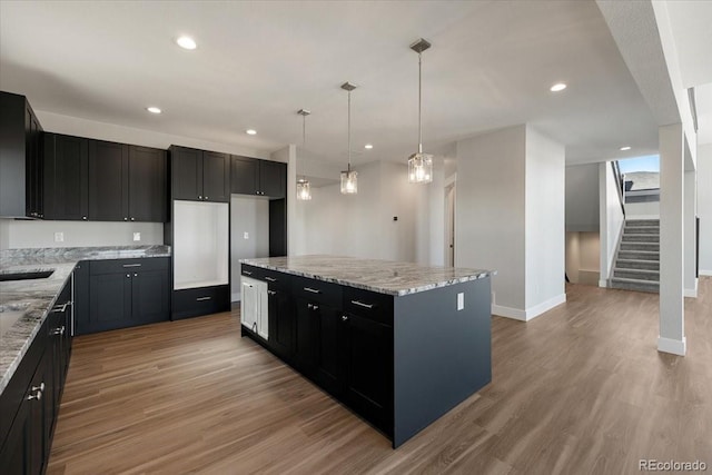 kitchen with decorative light fixtures, light hardwood / wood-style flooring, light stone countertops, and a center island