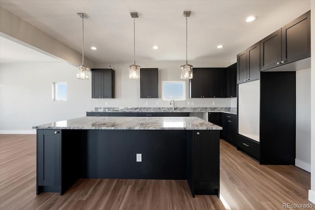 kitchen with light stone counters, a kitchen island, light hardwood / wood-style floors, and hanging light fixtures