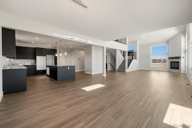 unfurnished living room with dark wood-type flooring, a stone fireplace, and sink