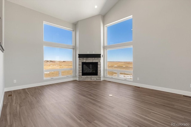 unfurnished living room with a stone fireplace, a towering ceiling, and hardwood / wood-style floors