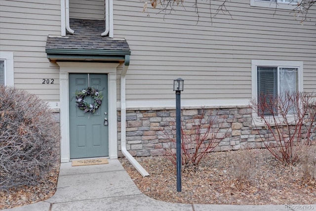 view of exterior entry featuring stone siding and roof with shingles