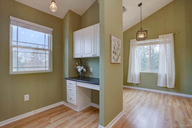 kitchen featuring a healthy amount of sunlight, vaulted ceiling, built in desk, and white cabinetry