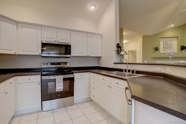 kitchen with lofted ceiling, stainless steel appliances, a sink, white cabinetry, and dark countertops